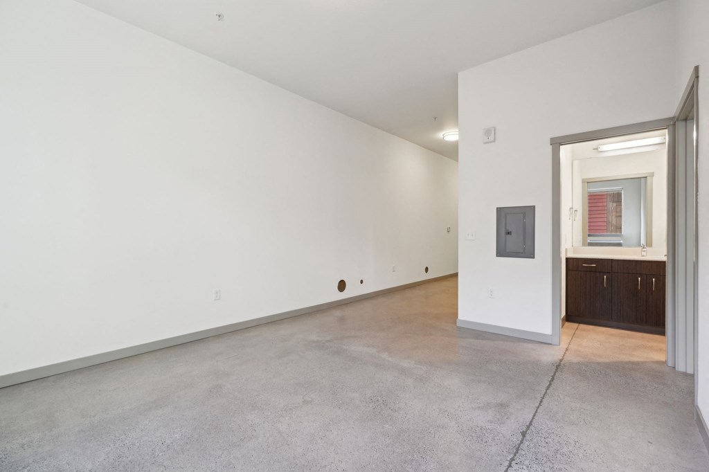 A large empty room with a doorway leading to a kitchen area.