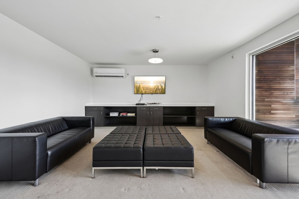 A black leather couch and ottoman are in a white room with a television.