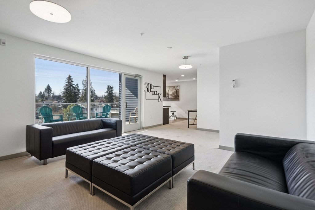A black leather couch sits in a bright room with a large window.