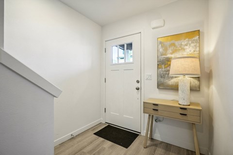 A white door is in a hallway with a lamp and a painting on the wall.