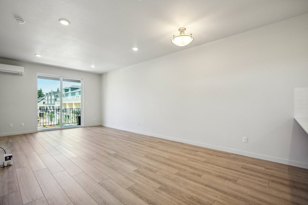 the living room is spacious and has a large window and hardwood flooring