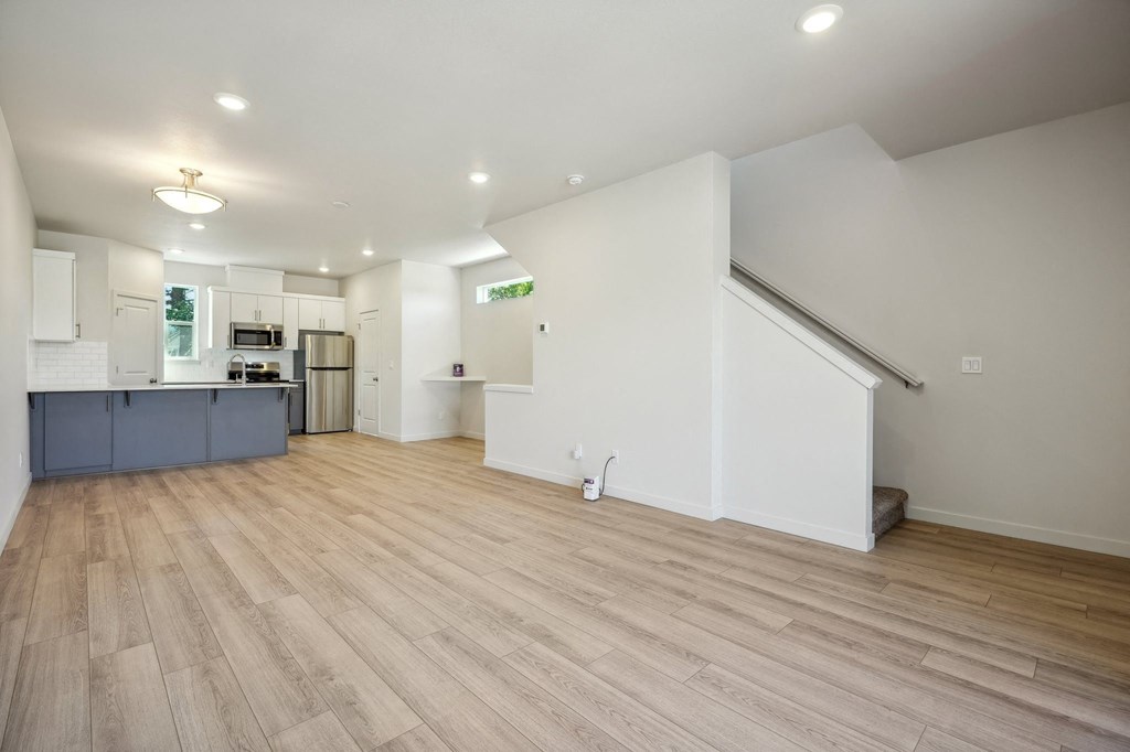 the living room and kitchen of a house with white walls and wood floors