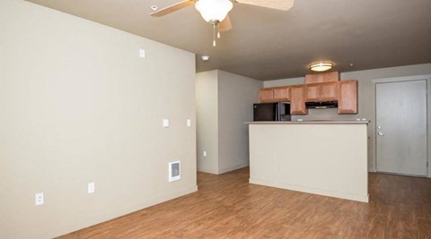 an empty living room with a kitchen and a ceiling fan