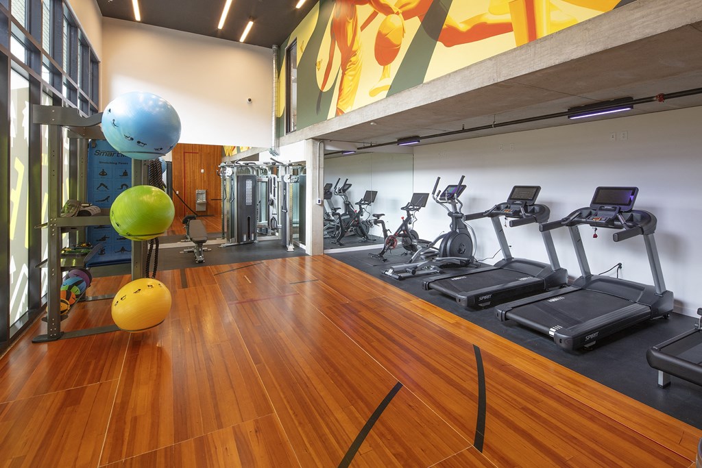 a gym with cardio equipment and weights on a wooden floor at The Weidler in Portland, OR 97209