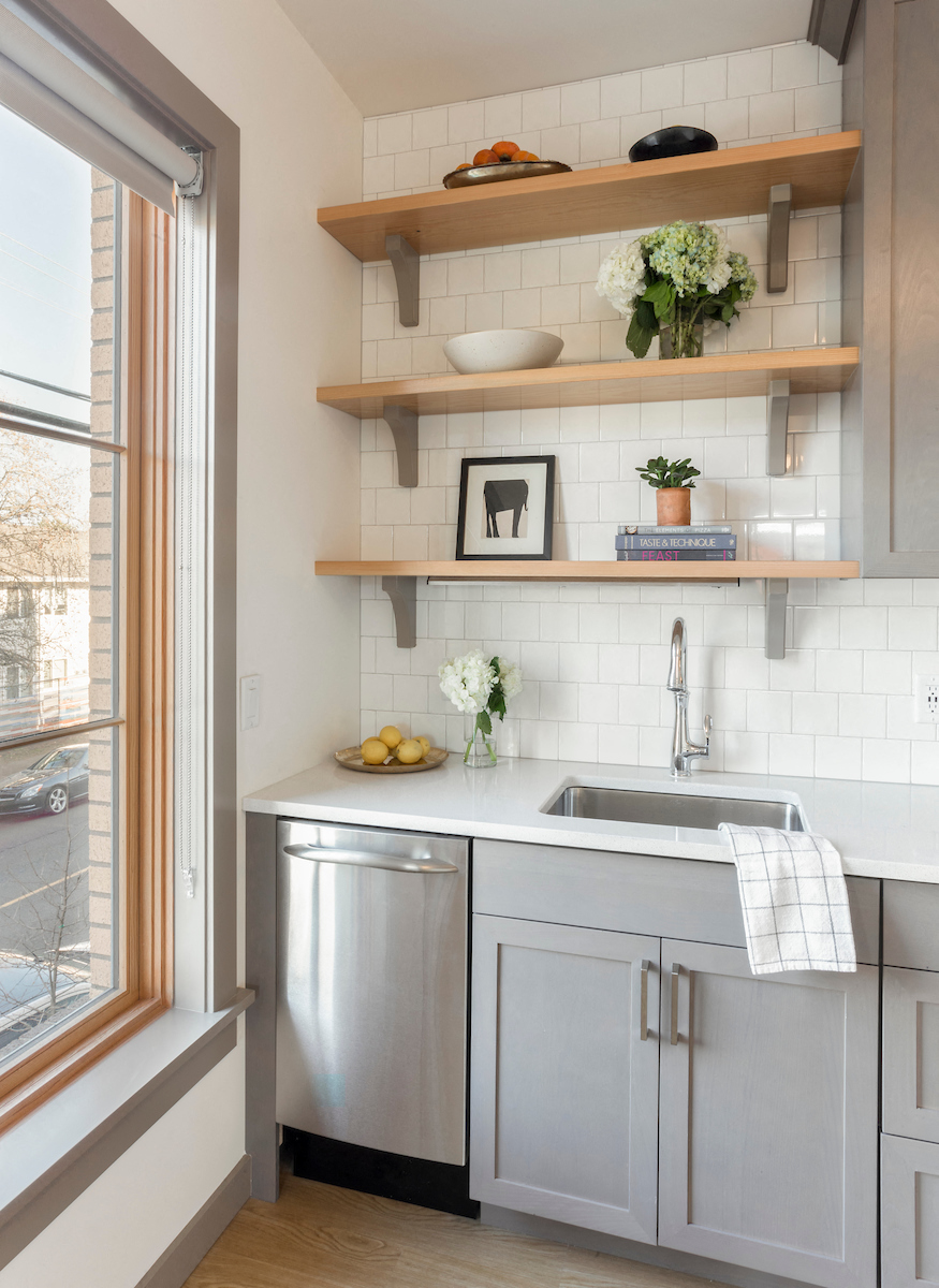 A kitchen with a stainless steel dishwasher and wooden shelves above the sink.