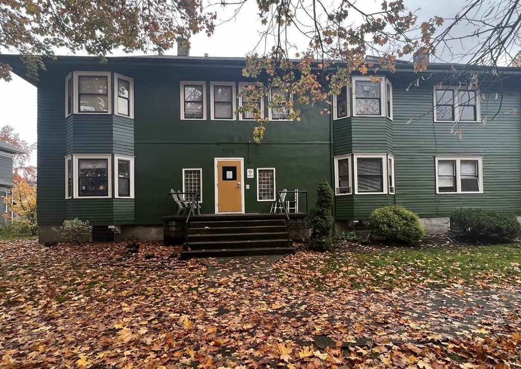 A green house with a yellow door and white windows.