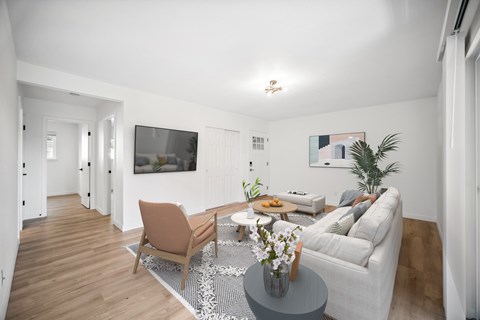 A living room with a grey couch, a brown chair, a coffee table with a vase of flowers, and a flat-screen TV mounted on the wall.