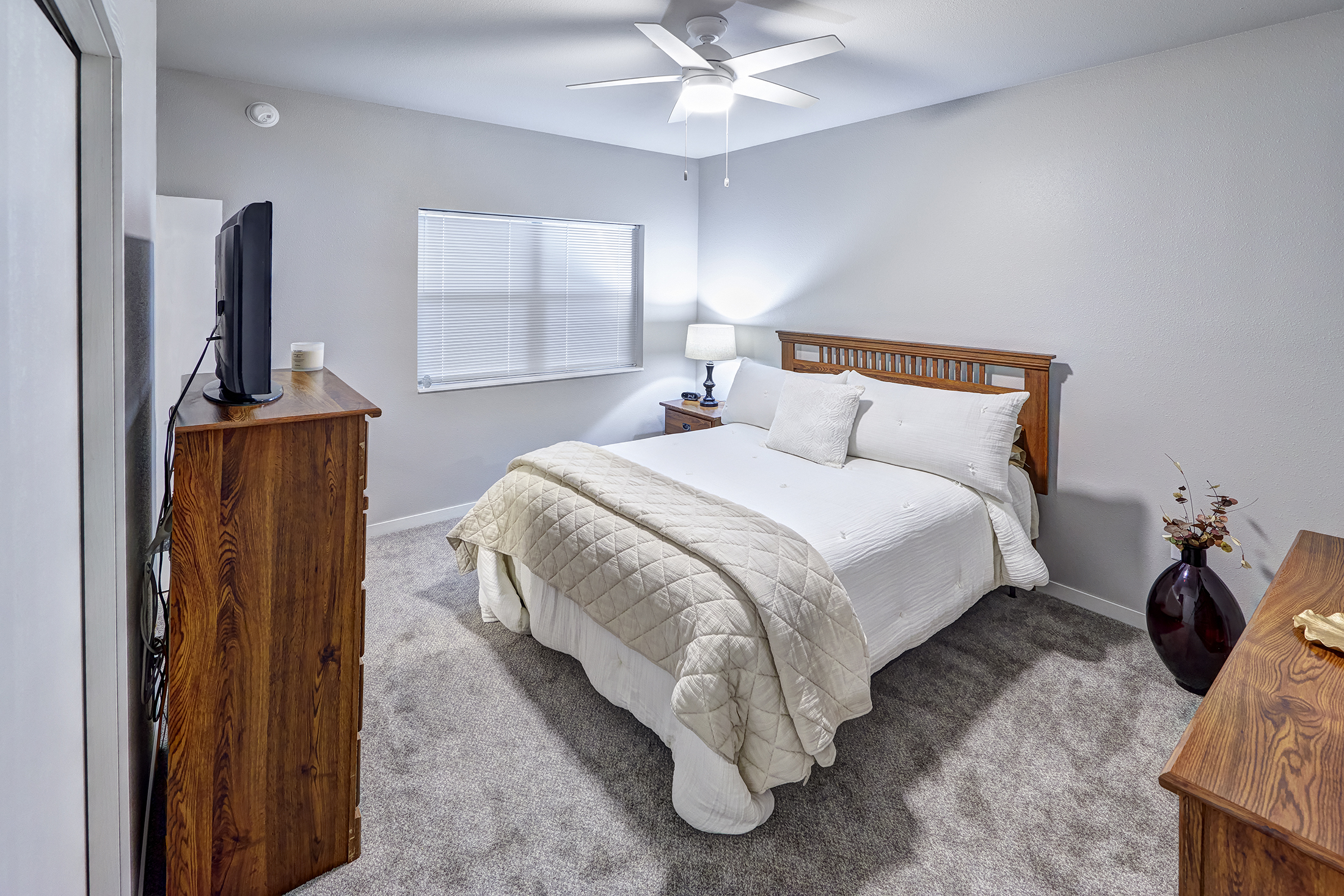 A bedroom with a bed, dresser, and ceiling fan.