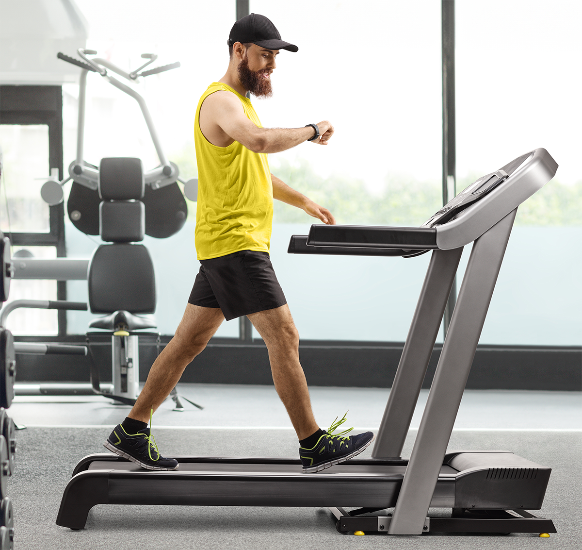A man in a yellow shirt and black shorts is running on a treadmill in a gym.