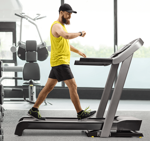 A man in a yellow shirt and black shorts is running on a treadmill in a gym.