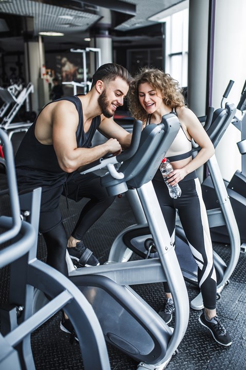 A man and a woman are working out on exercise machines in a gym.