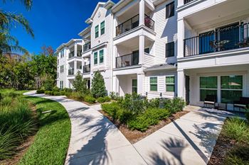 A white apartment building with green bushes and a walkway in front