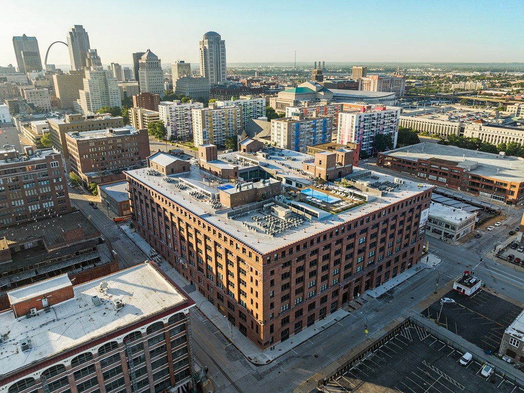 a large brick building with a white roof with a city skyline in the background