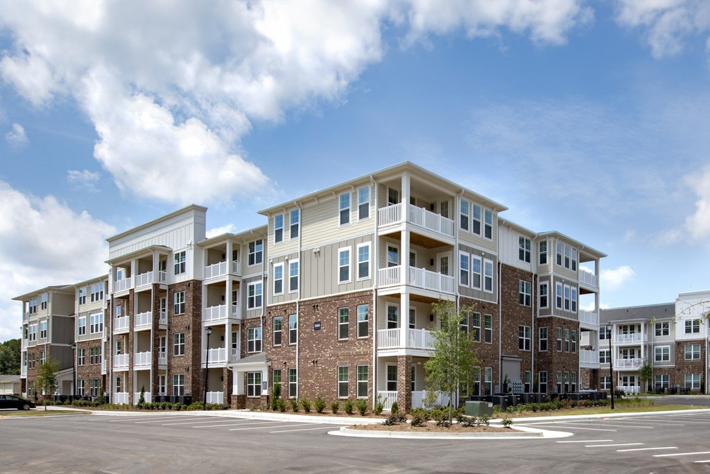 Pet-Friendly Apartments in Norcross - The Darnell - Building Exterior with Streetview, with Parking Spots, Brick Details, and White Balconies Visible
