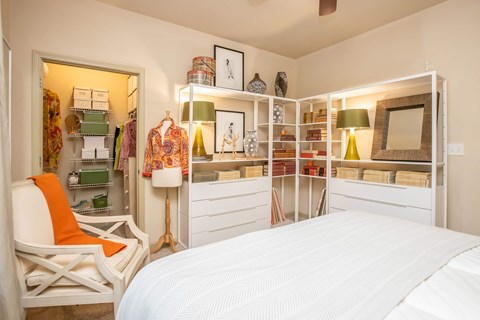A bedroom with a white bed and a chair with an orange cushion.