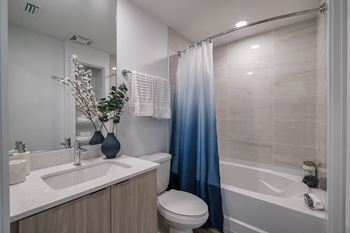 A bathroom with a white sink, a toilet, a bathtub, and a blue shower curtain. at Altis Santa Barbara, Florida
