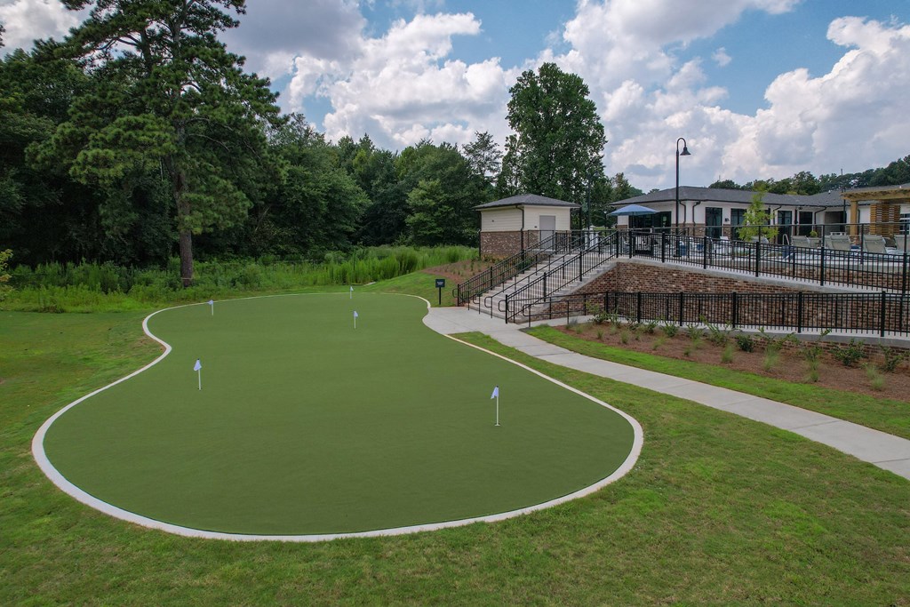 a synthetic turf putting green with a clubhouse and pavilion in the background