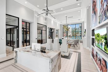 A modern office lobby with a reception desk and a large screen on the wall.