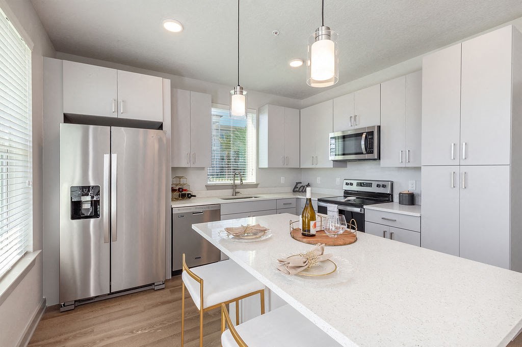Dog-Friendly Apartments In Daytona Beach - Madison Pointe - Kitchen With Sleek White Cabinets, Island With Barstools, And Stainless Steel Appliances.
