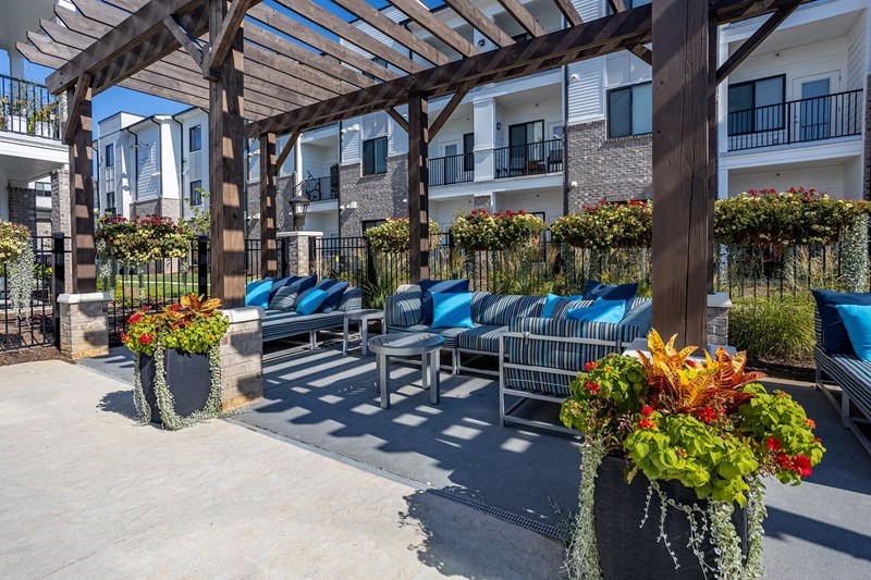 an outdoor lounge area with chairs and tables under a wooden pergola