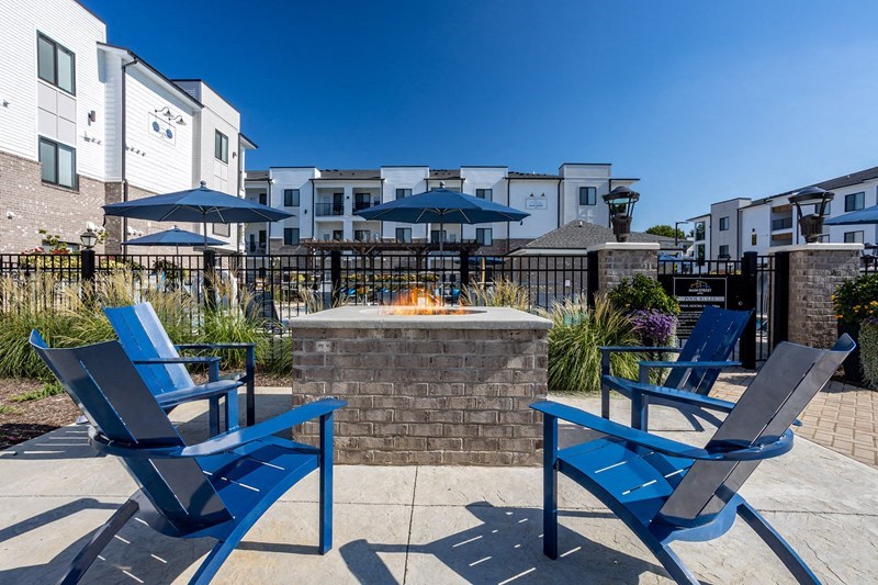 a fire pit with blue chairs and umbrellas in front of an apartment building