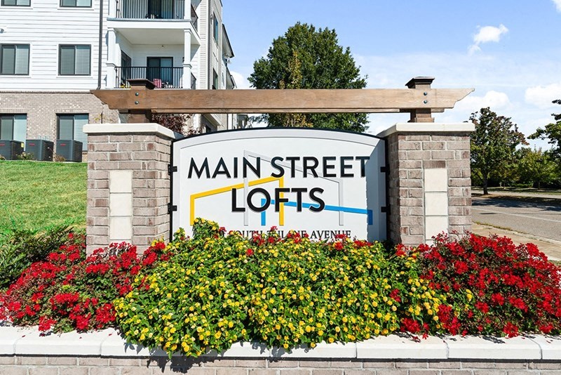a sign for main street lofts in front of flowers