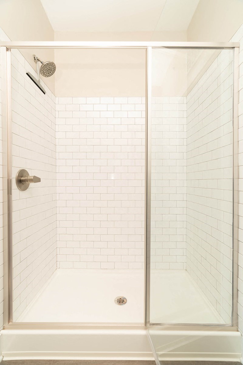 a bathroom with a shower with white tiles and a glass door