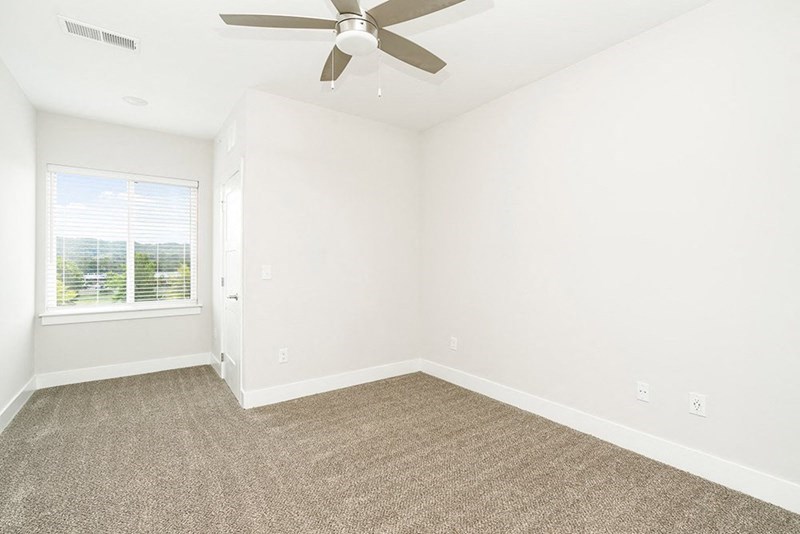 an empty living room with a ceiling fan and a window