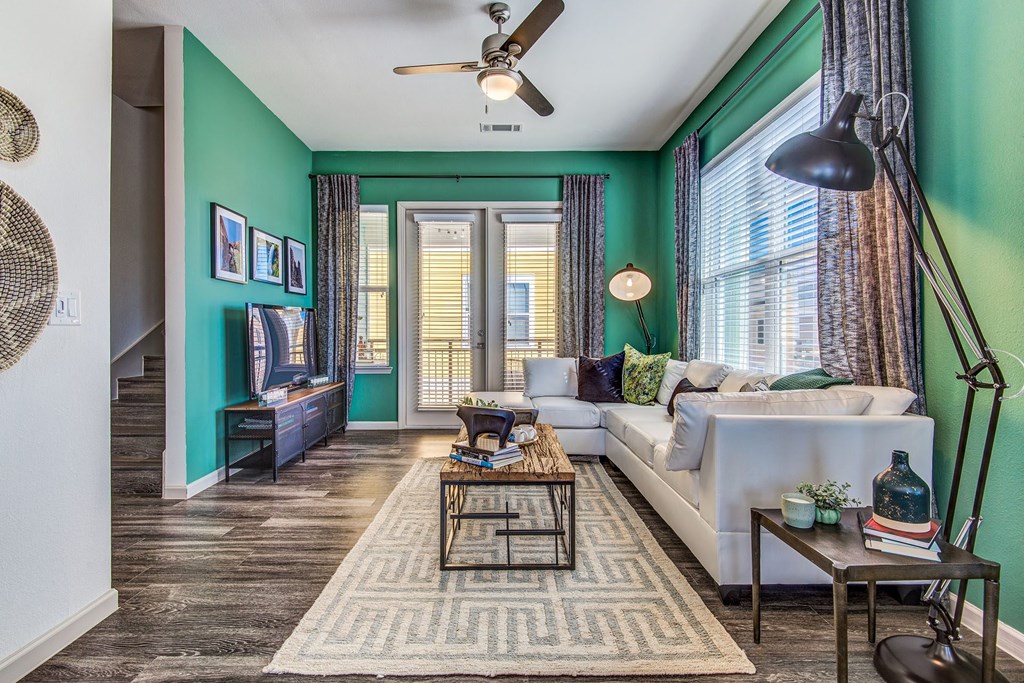 Dog Friendly Apartments in Lewisville, TX - Hebron 121 Station - Open Space Living Room with Hardwood Floors, Green Accent Walls, Ceiling Fan, Stylish Interiors, and Door that Leads to a Balcony.