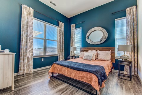 Apartments for Rent in Lewisville - Hebron 121 Station - Spacious Bedroom with Stylish Decor, Wood-Style Flooring, Large Windows, Two-Toned Walls, Bed, Nightstand, Lamps, and Dresser.