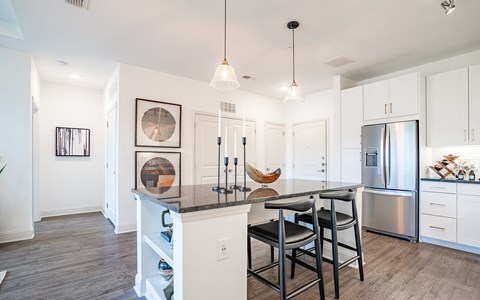 a kitchen with a large island with stools and a stainless steel refrigerator