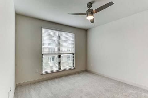an empty living room with a large window and a ceiling fan