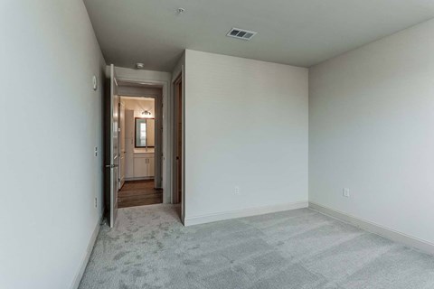 an empty living room with white walls and a hallway to a bathroom