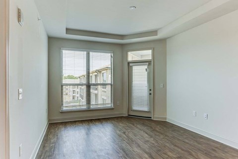an empty living room with a large window and a door to a balcony