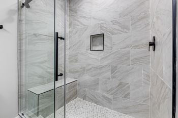 A bathroom with a glass shower door and marble tiles.