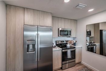 A modern kitchen with a stainless steel refrigerator and wooden cabinets at Altis Santa Barbara, Florida