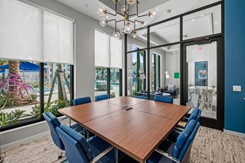 A conference room with a long table and chairs, a chandelier, and a view of the outside through the windows.