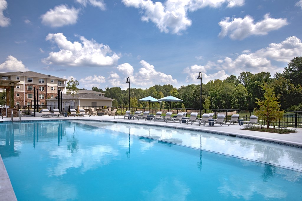 a swimming pool with chaise lounge chairs and umbrellas with a building in the background
