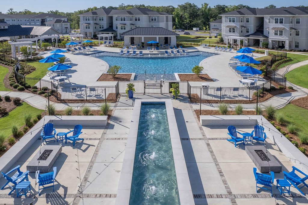 a swimming pool with lounge chairs and umbrellas in front of an apartment complex