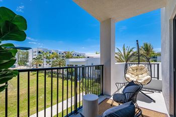A balcony with a chair and a table overlooking a building and palm trees at Altis Santa Barbara, Florida