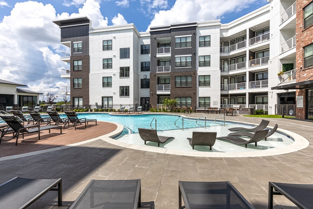 a swimming pool with lounge chairs in front of an apartment building