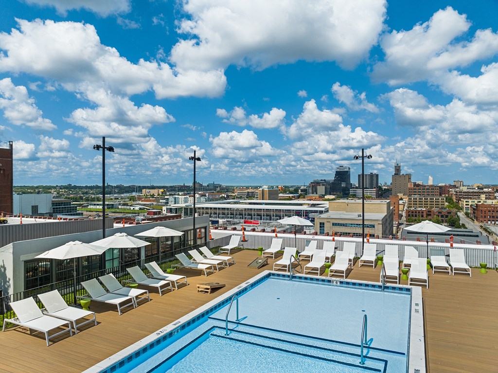 a rooftop pool with lounge chairs and umbrellas and a city in the background