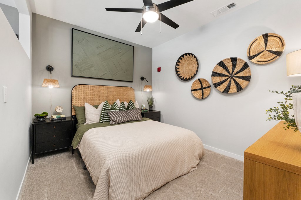 One-Bedroom Luxury Apartments in Huntsville, AL - The Arcadia - Bedroom with Plush Carpeting, Bed, Nightstands with Drawers, Dresser, Wall Decorations, and Ceiling Fan.
