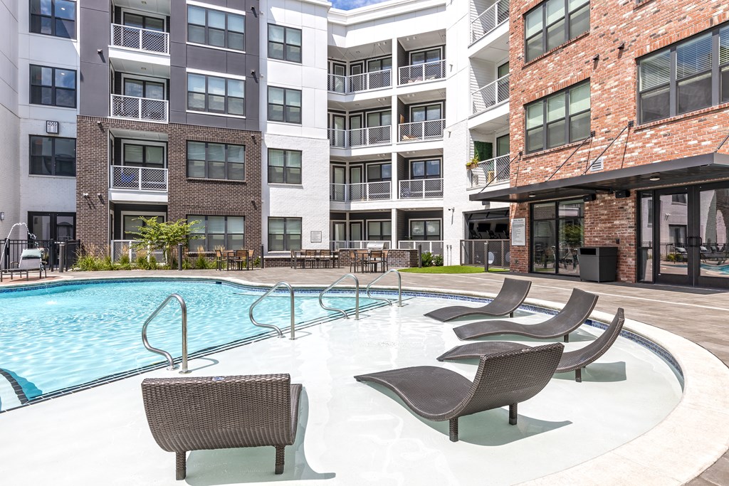 a swimming pool with chairs in front of an apartment building