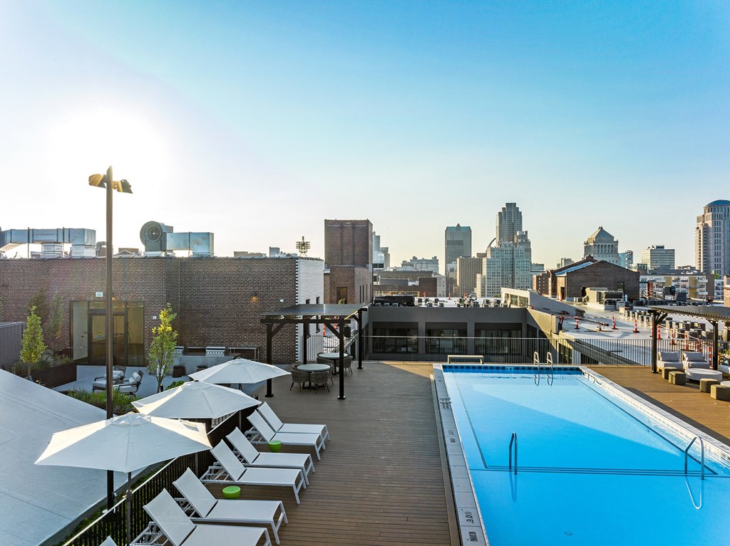 a rooftop pool with lounge chairs and umbrellas and a city skyline in the background