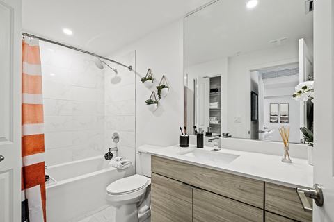 a bathroom with white walls and a white toilet next to a bathtub with a shower curtain at Altis Blue Lake, Lake Worth, FL