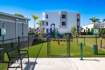 A playground area with a slide, swings, and a bench in front of a white building.