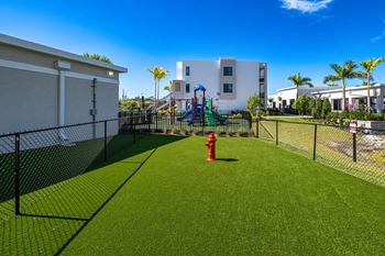 A playground with a red fire hydrant in the middle of a green lawn.