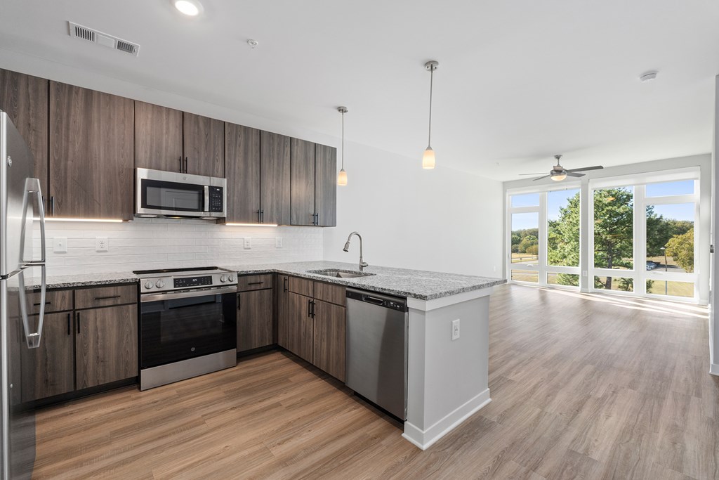 Upscale Apartments in Huntsville, AL - The Arcadia - Kitchen with Luxury Vinyl Plank Flooring, Peninsula, Pendant Lights, Granite Countertops, Stainless-Steel Appliances, and View of Living Area.