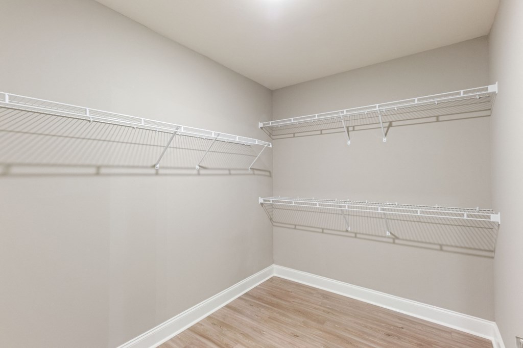 an empty closet with white shelves and a wood floor